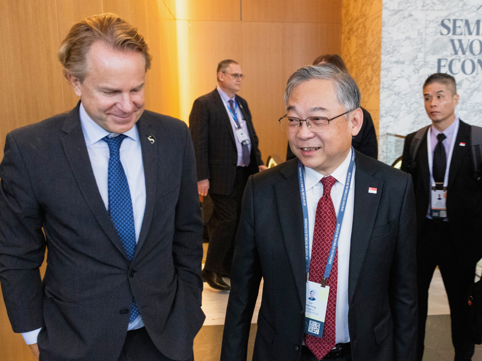 Two men talking while walking through a hallway at a Semafor World Economy event